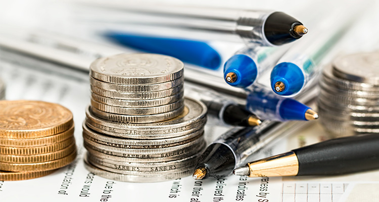 Close-up of two stacks of coins and several pens, posed meticulously.